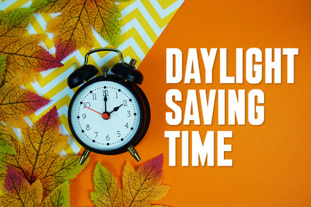 Daylight Saving Time with alarm clock and maple leaf decorated on orange backgroundの写真素材