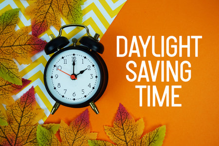 Daylight Saving Time with alarm clock and maple leaf decorated on orange backgroundの写真素材