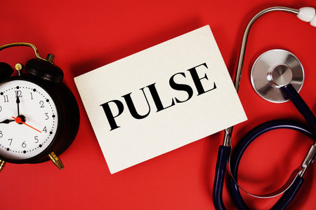 Pulse text written on paper card with stethoscope and alarm clock on red backgroundの写真素材