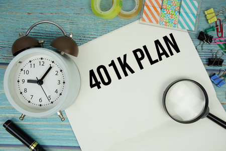 401K Plan text written on notepad with alarm clock and magnifying glass flat lay on wooden backgroundの写真素材