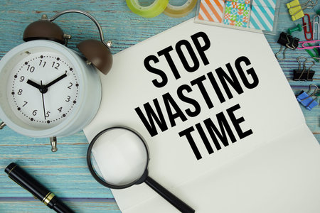 Stop Wasting Time text written on notepad with alarm clock and magnifying glass flat lay on wooden...