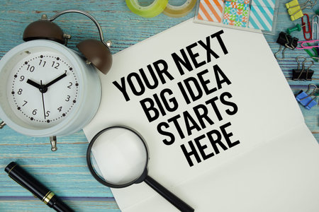 Your Next Big Idea Starts Here text on a paper surrounded by office supplies, a magnifying glass,...