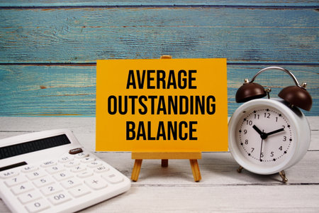 Average Outstanding Balance text written on paper card with calculator and alarm clock on wooden backgroundの写真素材