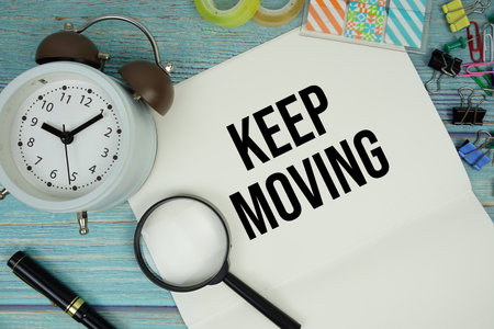 Keep Moving text written on notepad with alarm clock and magnifying glass flat lay on wooden backgroundの写真素材