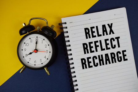 Relax Reflect Recharge text written on notepad with alarm clock on blue background