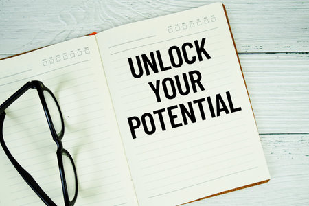 Notepad with message "Unlock Your Potential" and eyeglass on wooden backgroundの写真素材
