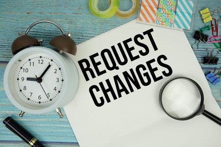 Request Changes text on a paper surrounded by office supplies, a magnifying glass, and a clock on a...