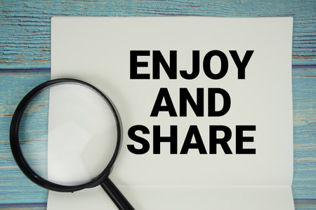 Enjoy And Share text written on notepad with magnifying glass flat lay on wooden backgroundの写真素材