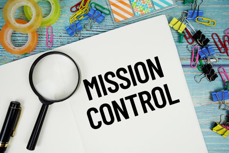 Mission Control text on a paper surrounded by office supplies and magnifying glass on a blue wooden surfaceの写真素材