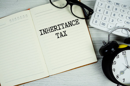 Inheritance Tax  text on notepad with alarm clock, eyeglasses and calculator on wooden backgroundの写真素材