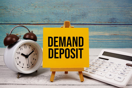 Demand Deposit text written on paper card with calculator and alarm clock on wooden backgroundの写真素材