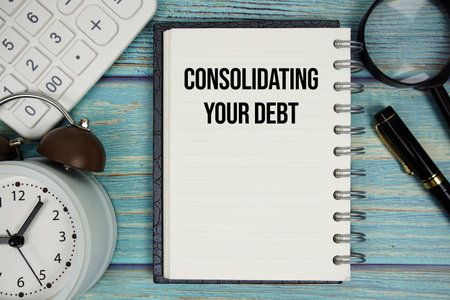 Consolidating Your Debt text on notepad with alarm clock, magnifying glass and calculator on wooden backgroundの写真素材