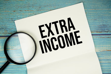 Extra Income text written on notepad with magnifying glass flat lay on wooden backgroundの写真素材