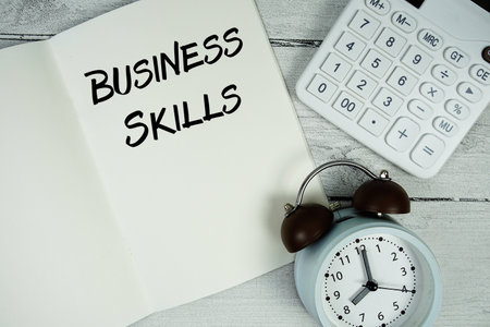Business Skills text on paper notebook page with alarm clock and calculator on wooden backgroundの写真素材