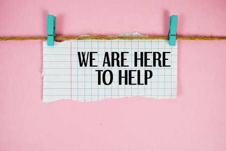 We Are Here To Help text written on rip paper with wooden clip on pink backgroundの写真素材