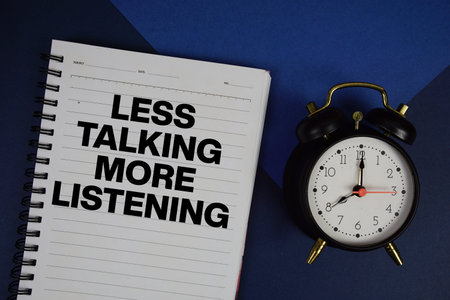 Less Talking More Listening text written on notepad with alarm clock on navy blue background