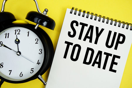 Stay Up To Date text with alarm clock flat lay on yellow background