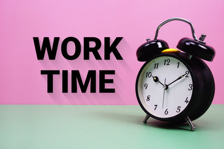 Black alarm clock on a pastel green and pink background with the text "Work Time"の写真素材