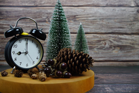Winter-themed decor with a vintage alarm clock, pinecones, and miniature snowy trees on a wooden surfaceの写真素材