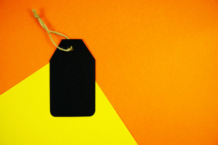 Black gift tag with twine resting on a bold orange and yellow background for Halloween labels, price tags, or seasonal promotions with space for custom text.の写真素材