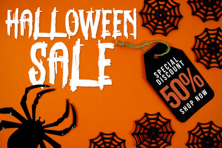 Happy Halloween Sale 50% Off with a large black spider, spiderwebs, and a bright orange background for Halloween celebrations, party invitations, or seasonal promotions.の写真素材