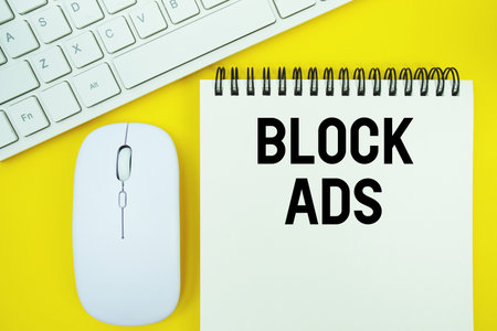 Notepad with the text "Block Ads" with white keyboard and wireless mouse on yellow backgroundの写真素材