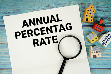 Notepad with APR Annual Percentage Rate with magnifying glass and house model on wooden background