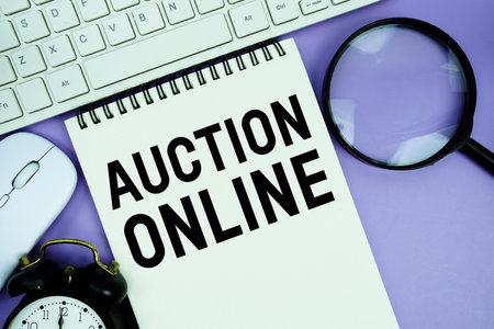 Notepad with the text "Online Auction" and white keyboard, wireless mouse, magnifying glass and alarm clockの写真素材