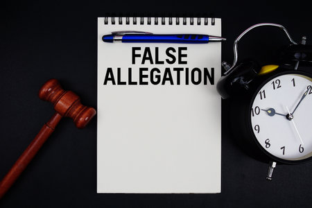False Allegation text written on notepad with gavel and alarm clock on black backgroundの写真素材