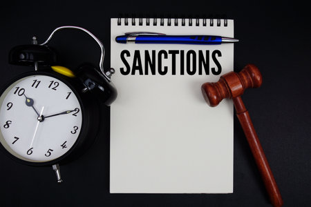 Sanctions text written on notepad with gavel and alarm clock on black backgroundの写真素材