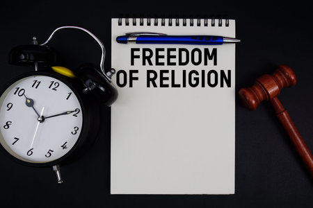 Freedom of Religion text written on notepad with gavel and alarm clock on black background