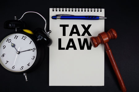 Tax law text written on notepad with gavel and alarm clock on black backgroundの写真素材