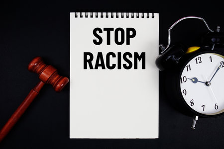 Stop Racism text written on notepad with gavel and alarm clock on black backgroundの写真素材