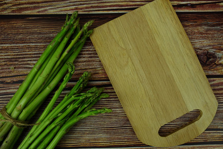 Bunch of fresh green asparagus stems with cutting wooden board on wooden backgroundの写真素材