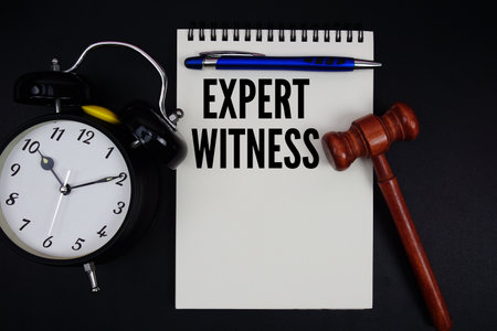 Expert Witness text written on notepad with gavel and alarm clock on black backgroundの写真素材