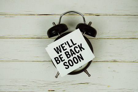 We'll Be Back Soon text with alarm clock on wooden backgroundの写真素材