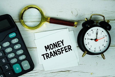 Money Transfer text with calculator, magnifying glass and alarm clock on wooden backgroundの写真素材
