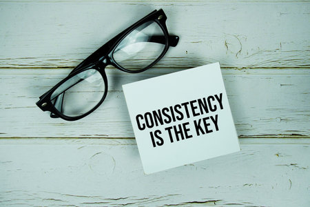 Consistency Is The Key text with eyeglasses on wooden backgroundの写真素材