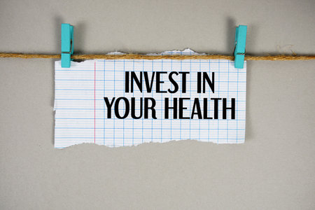 Invest In Your Health text written on rip paper with wooden clip on beige backgroundの写真素材