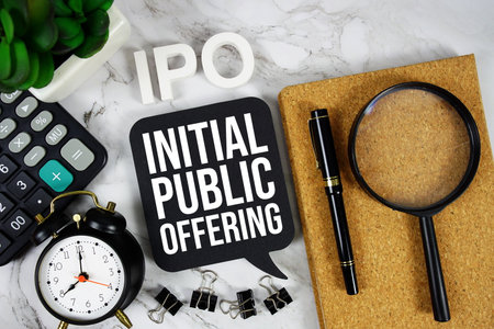IPO - Initial Public Offering acronym with calculator, alarm clock and magnifying glass, business concept backgroundの写真素材
