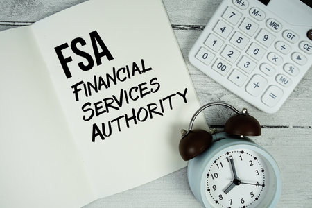 FSA Financial Services Authority text on paper notebook page with alarm clock and calculator on wooden backgroundの写真素材