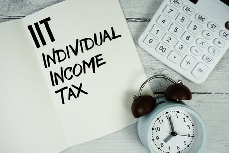IIT Individual Income Tax text on paper notebook page with alarm clock and calculator on wooden backgroundの写真素材