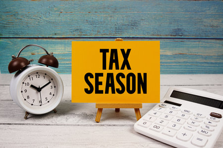 Tax Season text written on paper card with calculator and alarm clock on wooden backgroundの写真素材