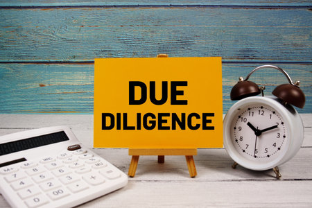 Due Diligence text written on paper card with calculator and alarm clock on wooden backgroundの写真素材