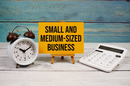 SMB Small and Medium-Sized Business text written on paper card with calculator and alarm clock on wooden backgroundの写真素材