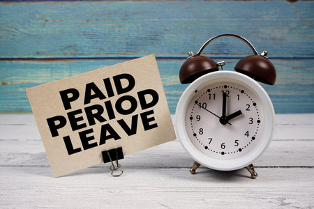 Paid Period Leave text written on paper card with alarm clock on wooden backgroundの写真素材