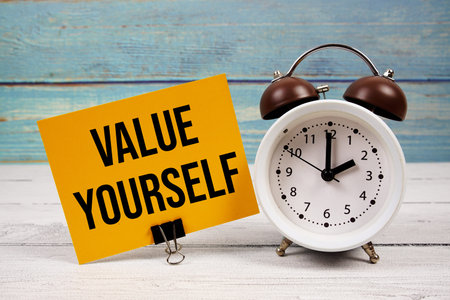 Value Yourself text written on paper card with alarm clock on wooden background