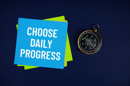 Choose Daily Progress text written on sticky note with compass on blue  backgroundの写真素材