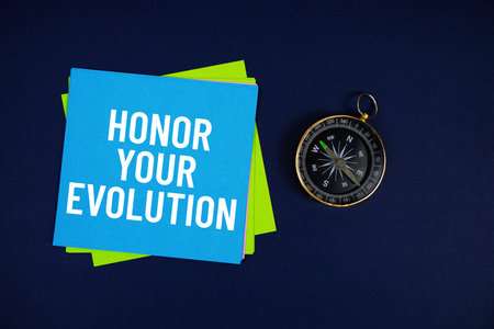 Honor Your Evolution text written on sticky note with compass on blue  background