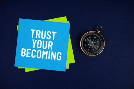 Trust Your Becoming text written on sticky note with compass on blue  backgroundの写真素材